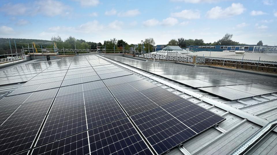 rows of solar panels on the roof of a building with a blue sky in the background