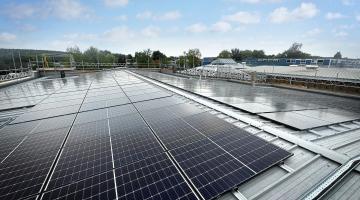 rows of solar panels on the roof of a building with a blue sky in the background