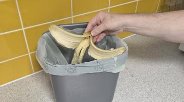 Someone putting a banana peel into a grey food waste caddie sitting atop the kitchen counter