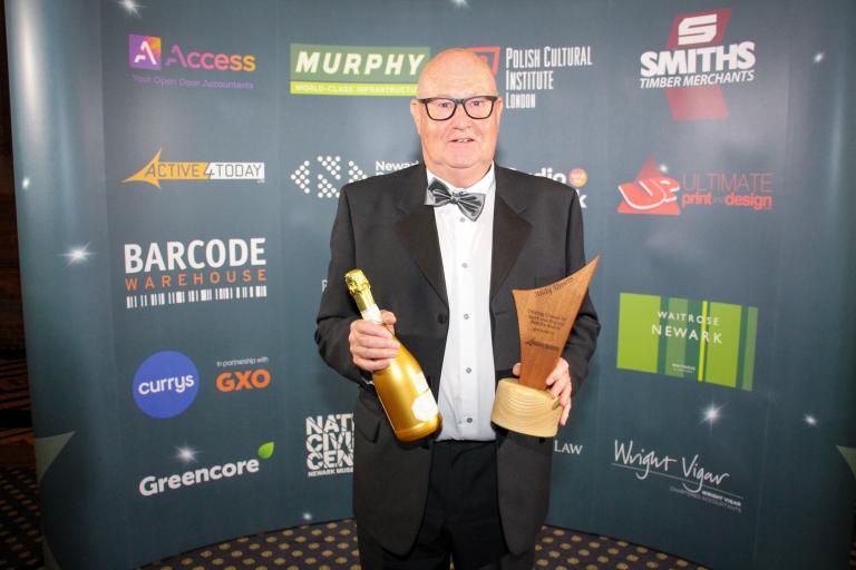 Andy Unwin smiling holding award trophy and prosecco bottle.