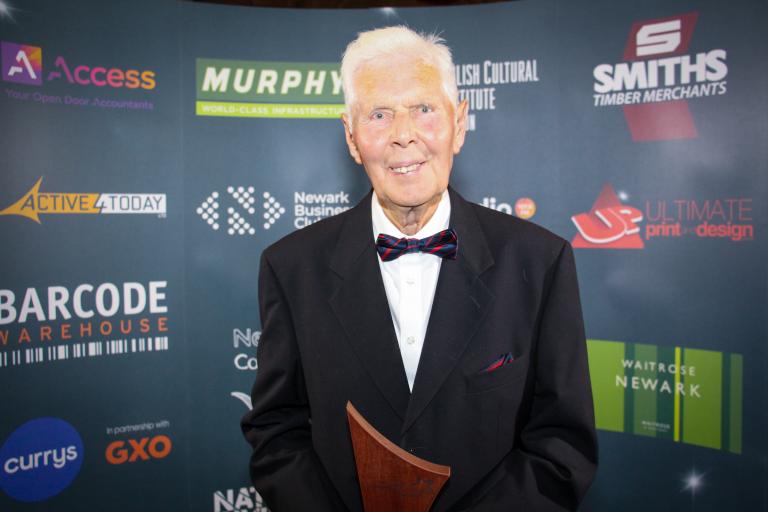 Terry Trickett smiling holding award trophy.