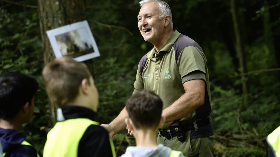 A park ranger talking to students in high vis jackets in a forest setting