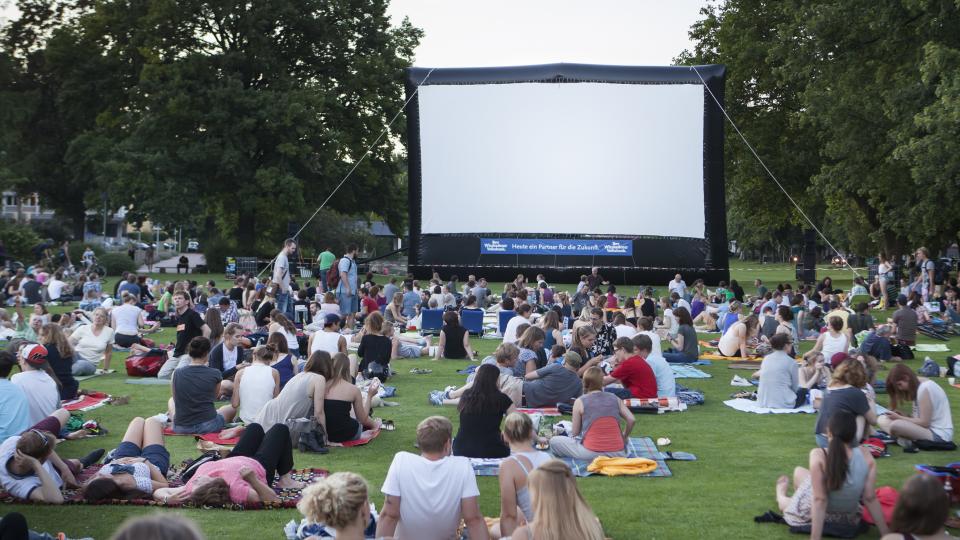 People sat around on picnic blankets outside watching an outdoor cinema screen