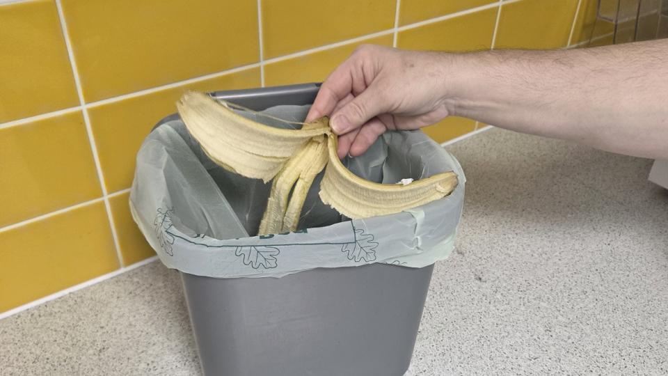 Someone putting a banana peel into a grey food waste caddie sitting atop the kitchen counter